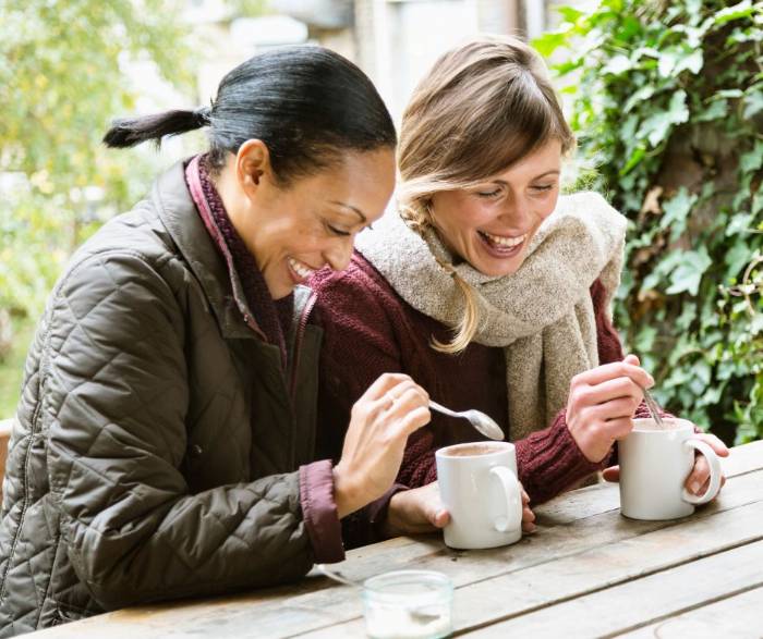 Two women smile while enjoying coffee with each other in a moment of happiness