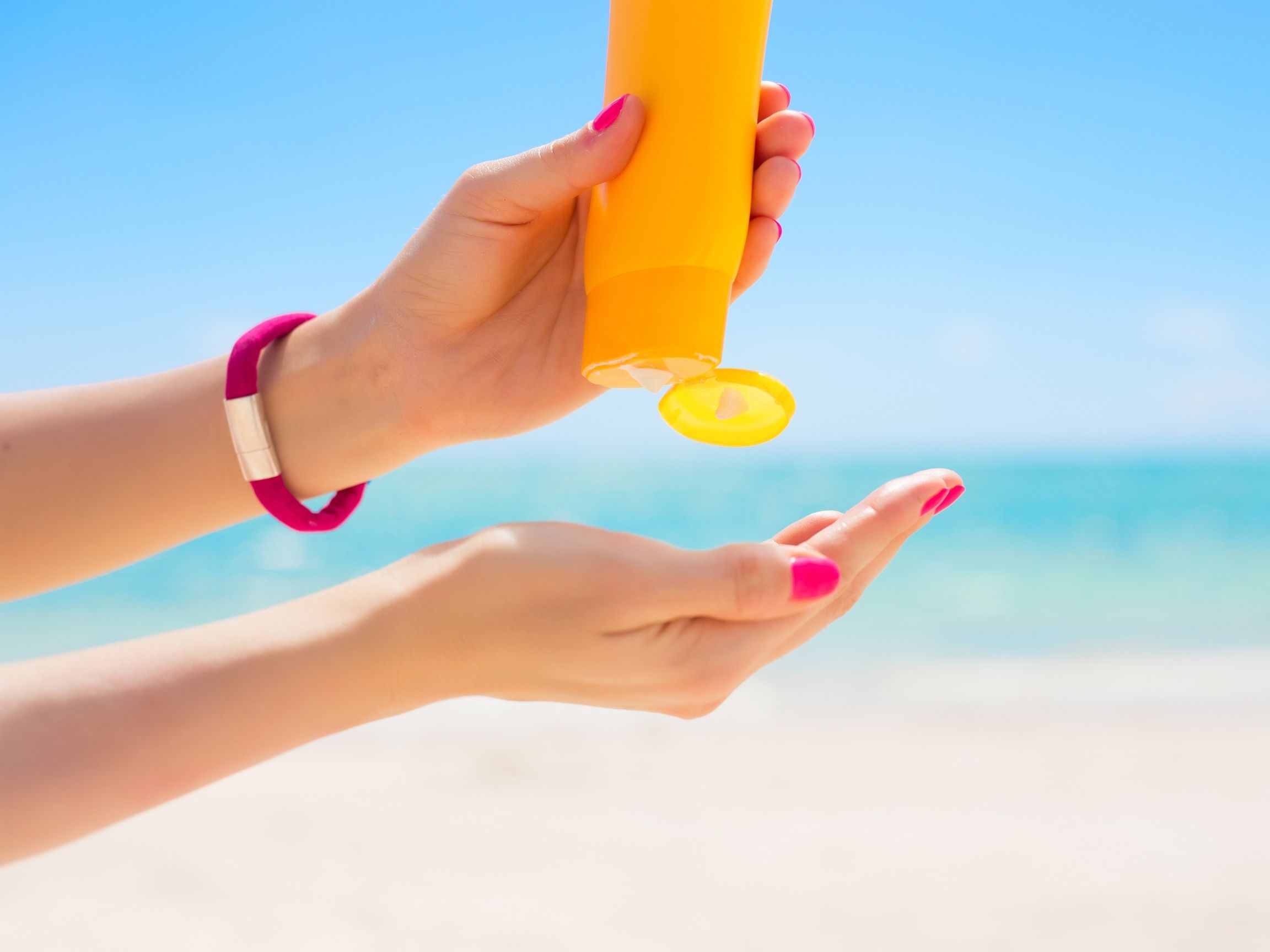 An open bottle of sunscreen pointed down into the palm of an open hand.