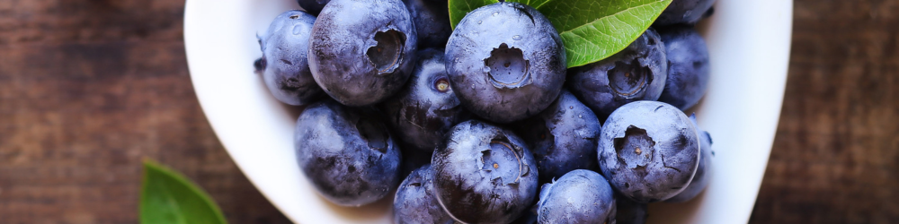 white bowl of fresh washed blueberries on wooden board