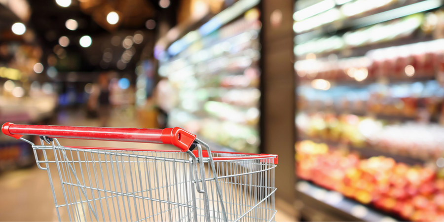 Supermarket grocery store with fruit and vegetable shelves interior defocused background with empty red shopping cart