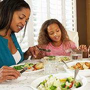 Family around the dinner table sharing a meal of steamed mixed vegetables (broccoli, cauliflower, carrots, and yellow peppers) and grilled boneless skinless chicken breast