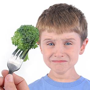 Boy in blue t-shirt with a disgusted look on his face being presented a broccoli floret on a fork