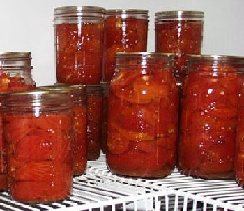 Several quart and pint size jars of bright red canned tomatoes sitting on a shelf.