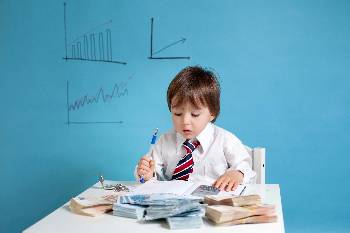 kids act as salespeople during fundraisers little boy in a suit at a table looking over budgets and money
