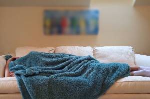 Person laying on couch with blanket over them 