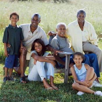 Multi-generation African American farm family sitting in a field around the patriarch of the family that is sitting in a chair. 