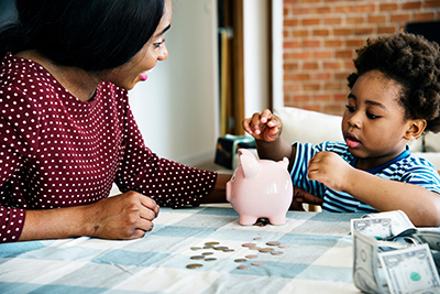 Teaching kids about money and savings African American mom and preschool-age son counting coins into a piggy bank
