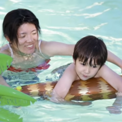 mom smiling in a pool helping her son swim