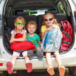Three children setting in back of SUV trunk.