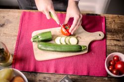 Vegetables Hands slicing a cucumber on a wooden cutting board.