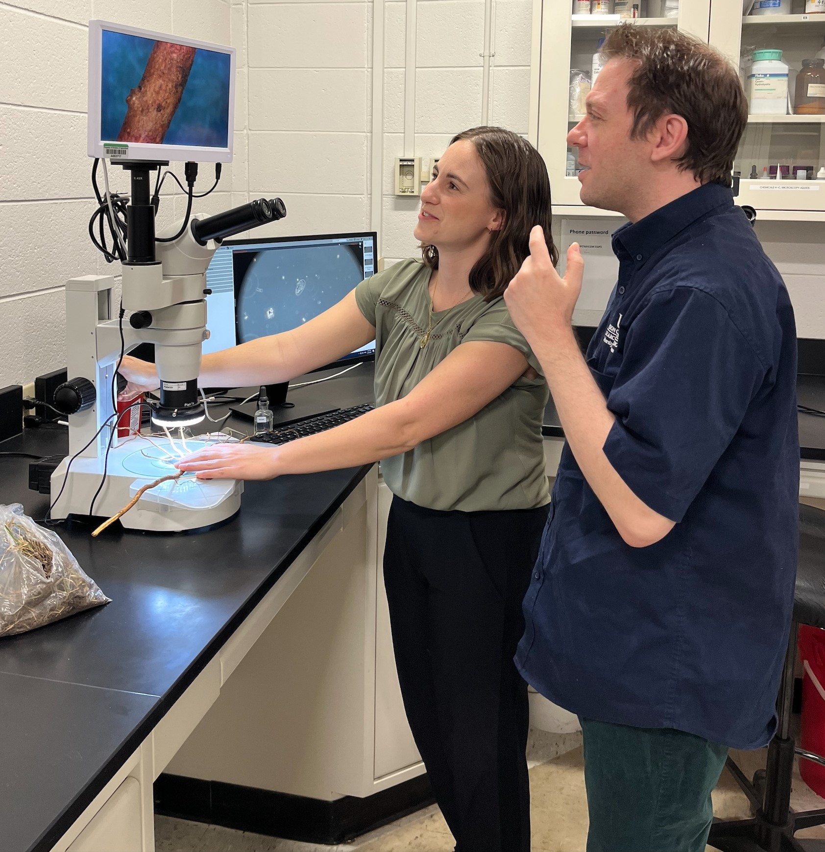 Taylor Klass (left) and Jason Pavel (right) inspecting roots under a dissecting microscope.